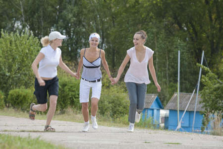 three young running girlfriends on the road smiling and holding hands together and having funの写真素材