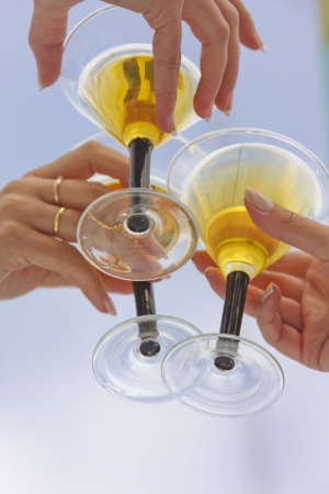 three female hands holding wineglasses with white wine over blue sky background. shot with studio strobe on location.の写真素材