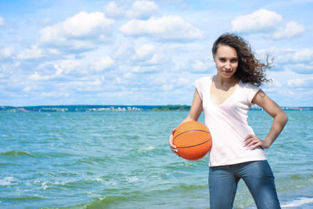 sporty and slim caucasian girl with curly natural hair holding orange ball near seasideの写真素材