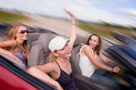 three happy and sensual caucasian girlfriends having drive on a red cabriolet car with bright positive expressions. shoot made on location with strobesの写真素材