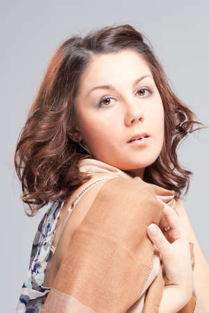 sensual pretty young brunette caucasian girl with languid facial expression standing with hands holding beige scarf isolatedの写真素材
