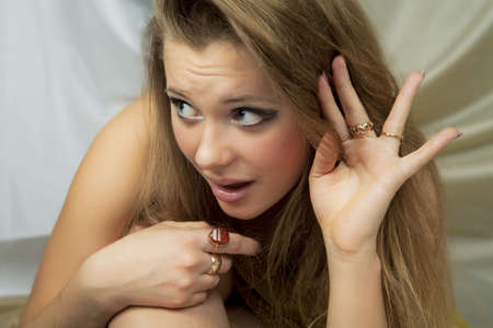 young caucasian blond girl sitting with body folded making surprised facial expresssion in front of textile backgroundの写真素材