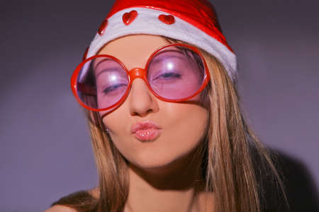 closeup portrait of a sensual caucasian blond girl in santa hat kissing in front of dark backgroundの写真素材