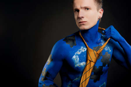 young handsome man with mozaic bodyart painting standing in front of black background: bodyart...