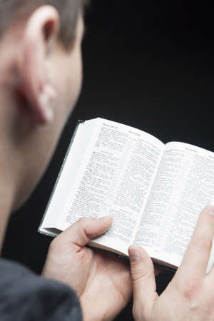 man reading bible standing against black background