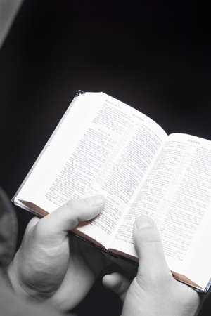 man holding bible over black background. desaturated picture