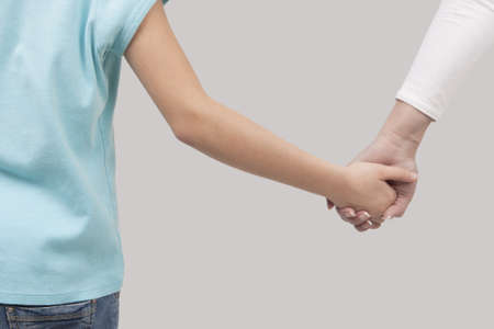 mother and her child standing connected via hands over light backgroundの写真素材