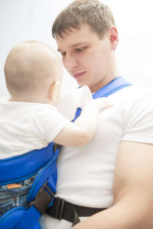 portrait of handsome father holding son in sling indoorsの写真素材