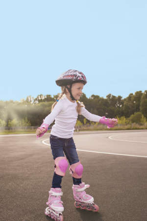 portrait of small little caucasian blond girl skating outside on stadium track in protective helmet