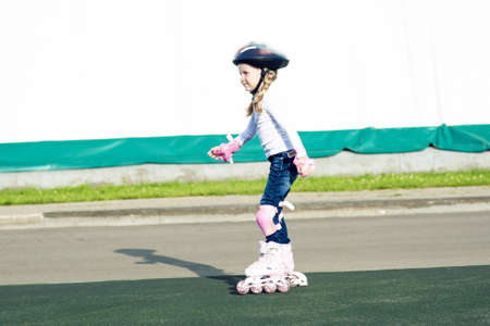 portrait of small little caucasian blond girl skating outside on stadium track in protective helmetの写真素材