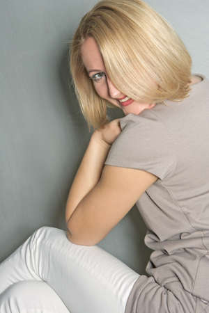 young blond caucasian woman sitting in front of gray wall and smilingの写真素材