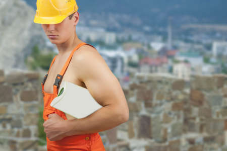 portrait of a strong builder handsome in protective helmet holding papers in hand over artistic backgroundの写真素材