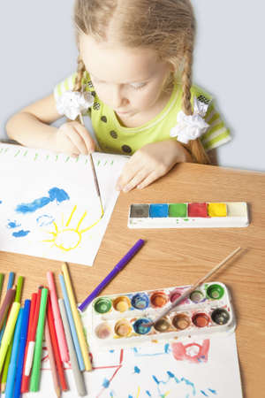 portrait of a little caucasian blond girl making drawing using colorful pencils  and paint indoors