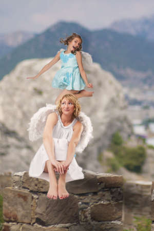 portrait of mother and daughter wearing angels wings together and having fun over artistic backgroundの写真素材