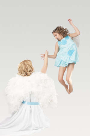 portrait of mother and daughter wearing angels wings together and having fun time jumping over grau backgroundの写真素材