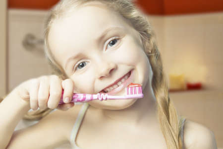 portrait of little smiling happy caucasian girl brushing her teeth standing indoorsの写真素材
