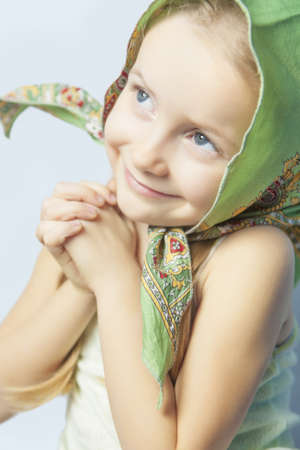 close up portrait of little cute caucasian girl in bright color scarf making gestures and holding hands togetherの写真素材