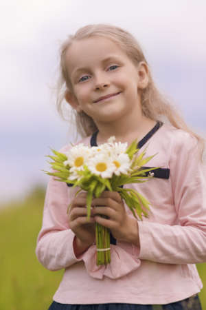 natural portrait of young little caucasian girl smiling and holding bunch of flowers outsideの写真素材