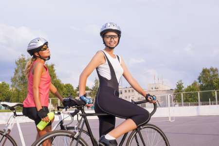 portrait of two young attractive females resting  with their race bikes and standing on a track. horizontal imageの写真素材