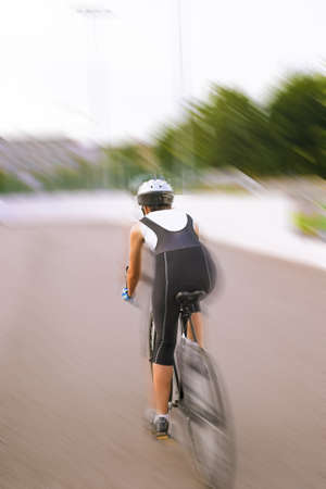 back of a female athlete cycling on a track. blurred motion, panning. vertical shotの写真素材