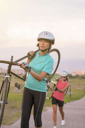 Portrait of Young Caucasian Sportswomen Work Out with Bicycle Outside. Vertical Image Orientation