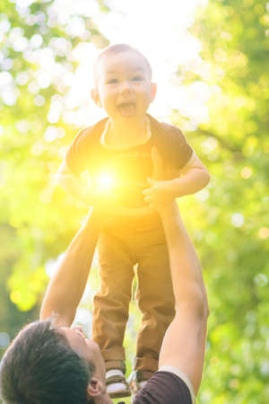 Portrait of Father Playing with His Son Outside by tossing his Up against Sun. Vertical Imageの写真素材