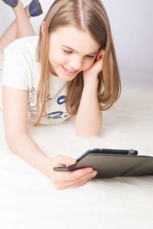 Pretty Little Caucasian Teenager Girl  Reading Digital E-book and Smiling. Over Gray Background. Vertical Imageの写真素材