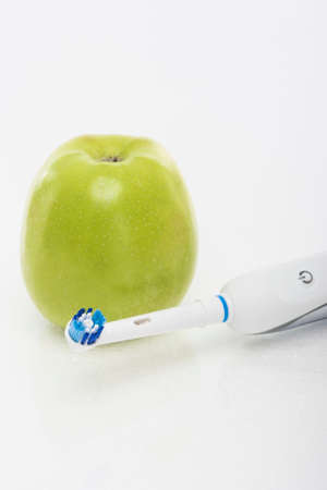 Dental Health Concept: Green Apple Together with Electric Toothbrush. Over White Background. Vertical Imageの写真素材