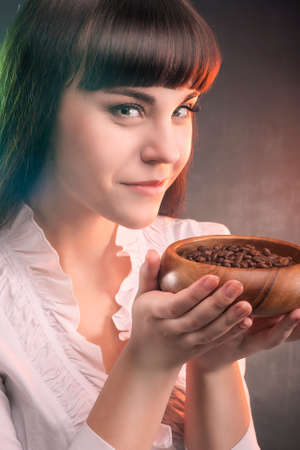 Cute Smiling Brunette Woman Holding Coffee Beans in Wooden Cup. Against Gray background. Vertical Imageの写真素材