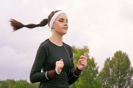 Jogging and Fiftenss Concepts: Portrait of Beautiful Caucasian Young Woman Jogging  and Listening to Music Outdoors. Horizontal Image Compositionの写真素材