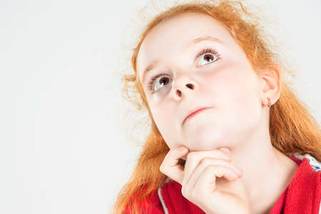 Thinking Red-haired Girl Looking Up and Touching Chin. Against White Background. Horizontal Image Composition.の写真素材