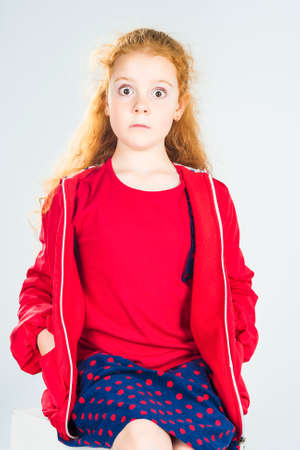 Portrait of Surprised Redhaired Caucasian Little Girl In Red Jacket and Polka dotted Skirt. Against White Background. Vertical Imageの写真素材