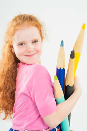 Cute and Happy Red-haired Caucasain Girl Playing with Huge Pencils. Posing Against White Background. Vertical Imageの写真素材