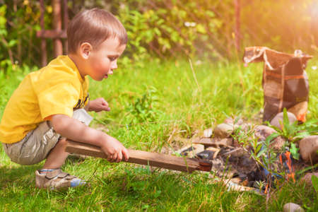 Caucasian Little Boy Dealing With Fire near Firepace Outdoors.の写真素材