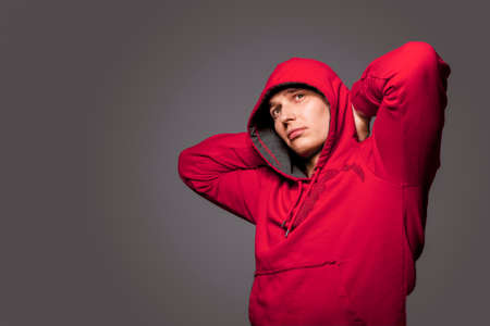 Portrait of Masculine Strong Tanned Caucasian Man in Red Hoody Jacket. Posing Against Gray Studio Backdrop. Horizontal Image Compositionの写真素材