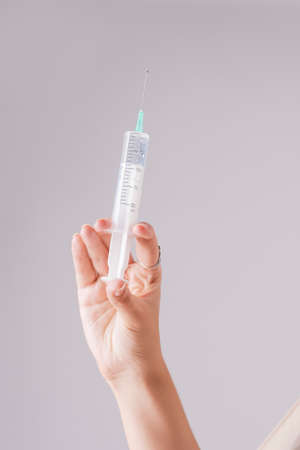 Closeup of Female Hand Holding Syringe with Transparent Liquid Inside. Over Gray Background....