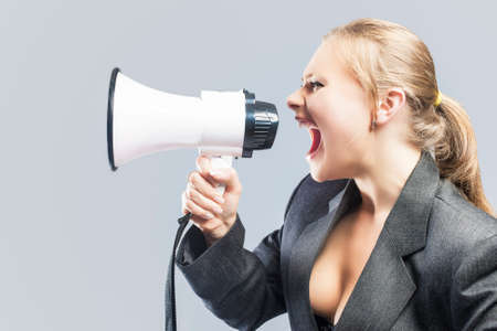 Sexy Furious Caucasian Blond Female in Lingerie and Suite Shouting Using Megaphone. Against Gray Background. Horizontal Imageの写真素材
