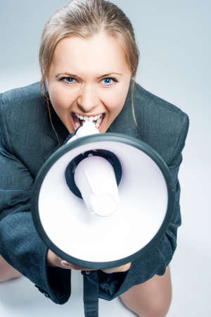 Sexy Caucasian Woman in Lingerie and Suite Screaming Using Megaphone. Sitting Against Gray Background. Vertical shotの写真素材