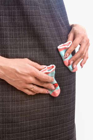 Pregnant Caucasian Woman Holding Small Size Socks for a Newborn Baby Over Her Stomach. Isolated On...