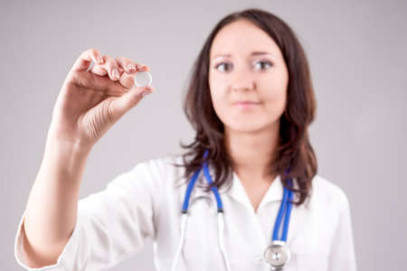 Medical Concept: Professional Female Caucasian Doctor Holding and Showing White Pill/Tablet.Posing Against Gray.Focus on The Pill. Horizontal Imageの写真素材