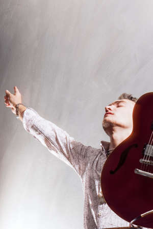 Praise and Worship Concepts. Young Caucasian Male Guitar Player Worshiping. Studio Shot. Against Gray. Vertical Imageの写真素材