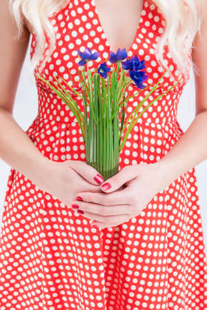 Closeup Of Hands Of Caucasian Female Woman in Red Polka Dotted Dress. Holding Bunch of Flowers in Hands in Front. Vertical Image Compositionの写真素材