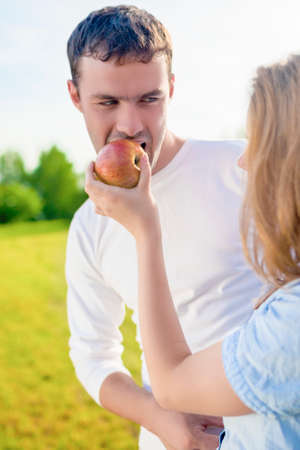 Lifestyle Concept and Ideas. Beauty Caucasian Female woman Feeding Handsome Man with Apple Fruit. Outdoor Activity. Vertical Image Compositionの写真素材
