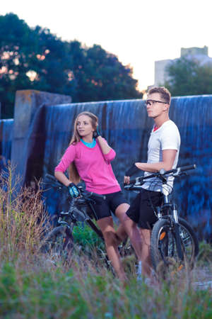 Two Caucasian Lovers With MTB Bicycles Outdoors. Posing Against Waterfall. Vertical Image Orientationの写真素材
