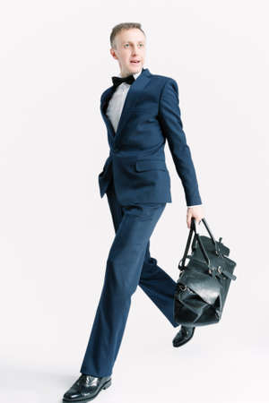 Business People Concepts. Young Caucasian Handsome Man With Bag Striding Against White. Vertical Image Orientationの写真素材