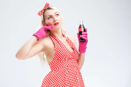 Pinup Retro Concepts. Dreaming Sexy Pinup Blond Woman With Bottle Posing in Polka Dotted Dress on White.Horizontal Image Orientationの写真素材