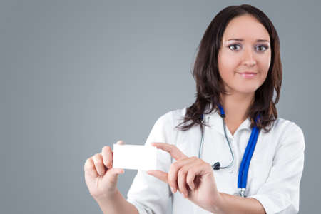Medical Female Doctor Presenting and Showing White Card for Product or Text. Caucasian Medical Professional Staff Posing Against Gray. Horizontal Imageの写真素材