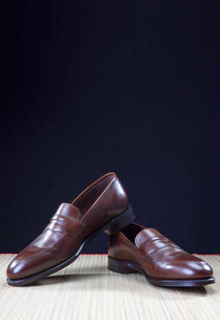 Shoes concepts. Men's Brown Stylish Penny Loafer Shoes On Straw Surface Against Black Background. Vertical Imageの写真素材