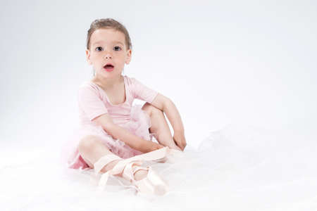 Cute Little Kid Posing as Ballerina. Putting Pointes on. Against White Background. Horizontal Image Compositionの写真素材
