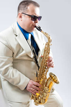 Expressive Stylish Caucasian Saxophone Player Performing in White Suit and Sunglasses in Studio. Vertical Imageの写真素材